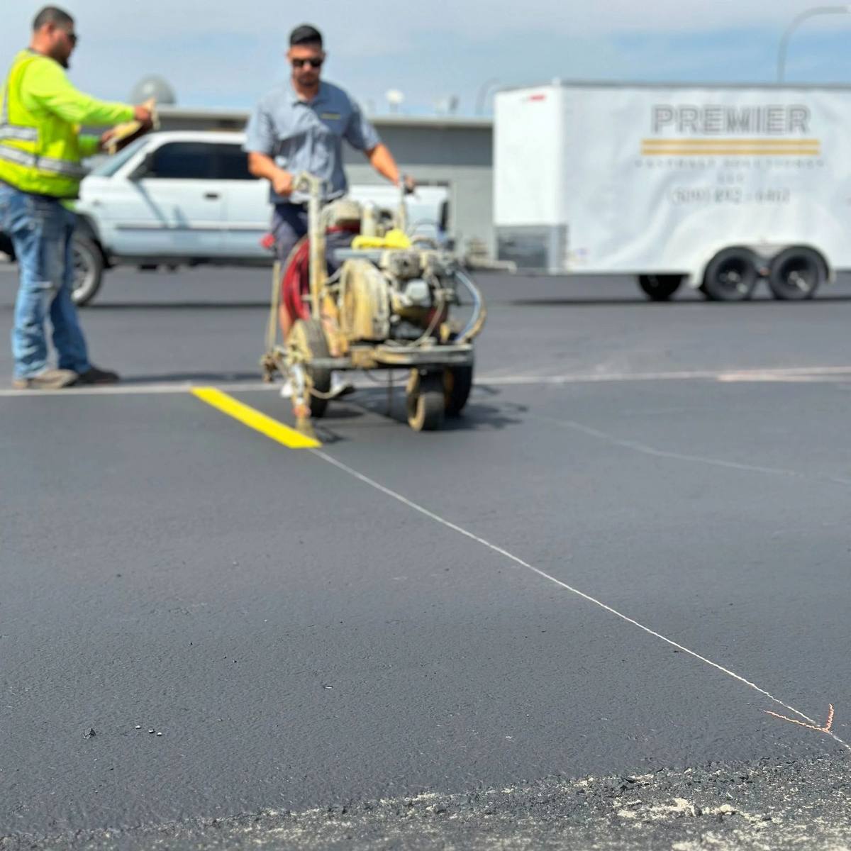 Asphalt maintenance in progress as sealcoat is spread across a parking lot surface